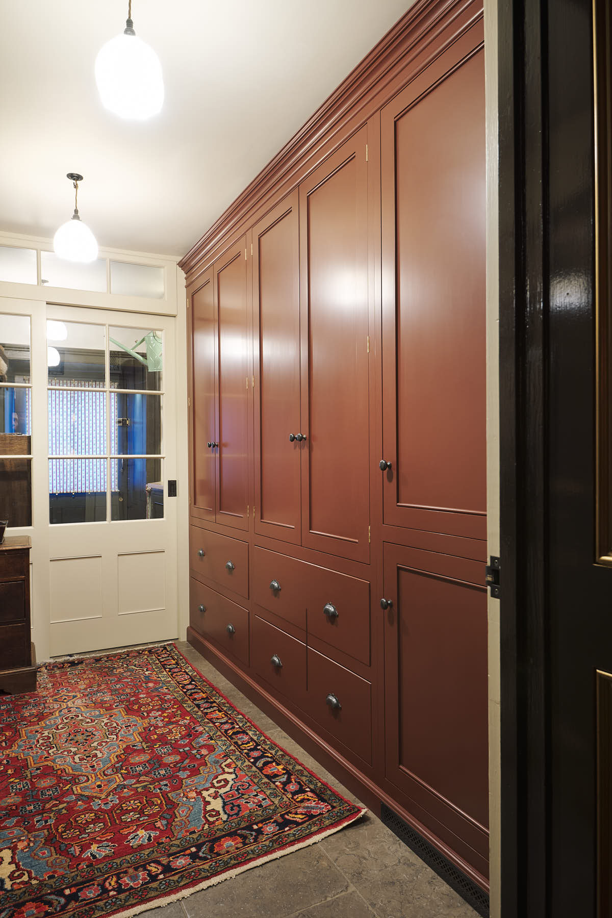 An oblique view of a practical Refectory red corridor with full-height cupboards and a large rug.