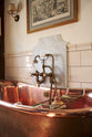 Behind a stunning copper bath, is a beautiful and practical cream subway splashback tiles.