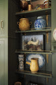 A closer look at the eccentric yet grand Bakehouse Green Classic English Kitchen’s shelves with the classic shelf brackets and aged brass railing. Pridefully displaying taxidermy, artisan ceramics, and collectable antiques, it embraces a unique museum-like social kitchen space.