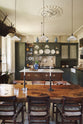 A quiet corner of an eccentric yet grand Bakehouse Green Classic English Kitchen features an L-shaped sink and cooker run with black granite worktop, a full-height cabinet, an overmantle with cream subway splashback tiles, and an Heirloom dairy table. Pridefully displaying taxidermy, artisan ceramics, and collectable antiques, it embraces a unique museum-like social kitchen space.