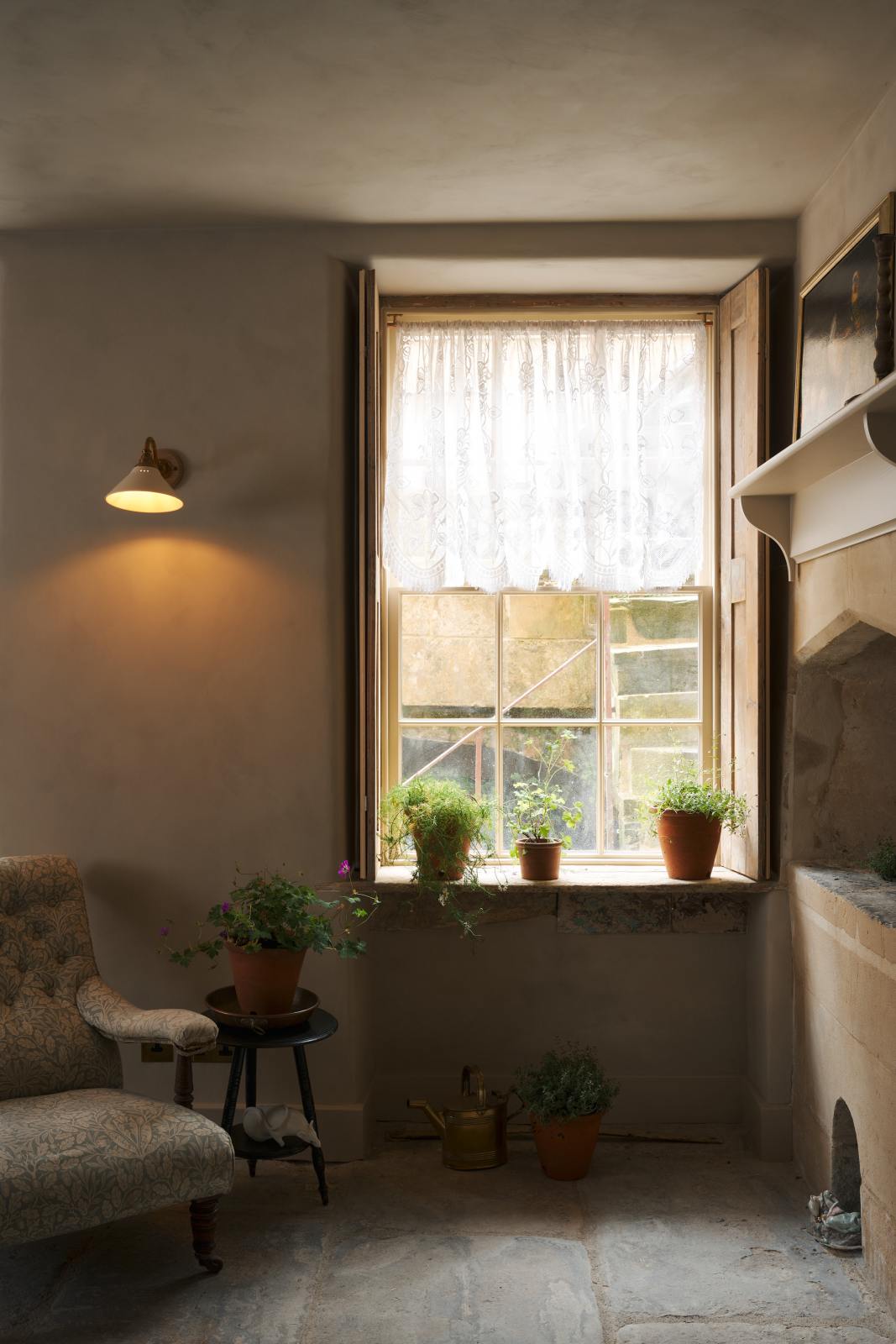 In the quiet corner of a rustic basement kitchen with sandy-coloured walls and ceiling, original Georgian detailing, cream doors and panelling with chipped paintwork and a worn stone floor. An heirloom wall light gently illuminated the ancient and preserved wall.