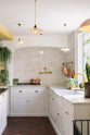This classic English kitchen features a white linen design, an L-shaped sink, and a Carrara marble countertop. It includes a large marble sink, an aged brass tap, a pot filler tap, and a white crackle metro tile splashback. Lush green hanging plants and white porcelain lights, with the original yellow beam, enhance the bright and cheerful atmosphere, making the kitchen lively and inviting.