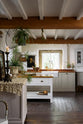 A beautiful white linen kitchen features a freestanding table, a kitchen run with a solid oak worktop, and a collection of vintage furniture and items reflecting the well-reserved historical space with its original plastered walls, wooden beams, and oak floors.