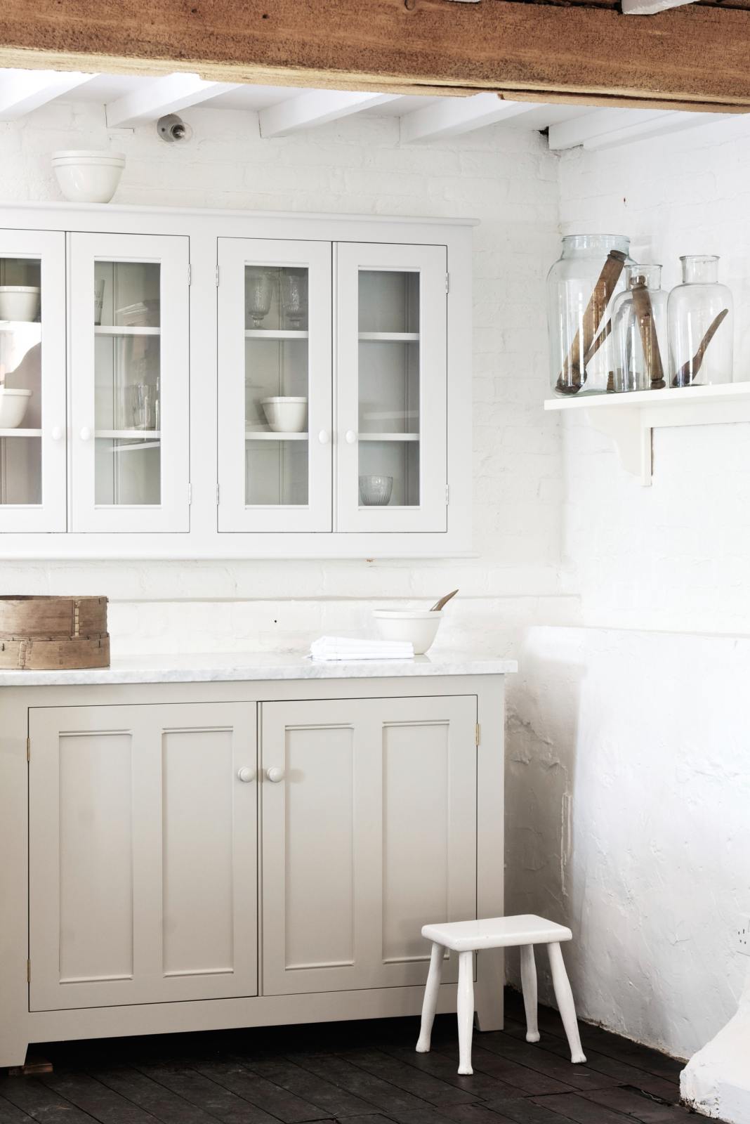 A beautiful white linen kitchen features a cooker run with a Carrara marble worktop, glazed wall cupboards, and a collection of vintage furniture and items reflecting on the well-reserved historical space with its original plastered walls, wooden beams and oak floors.