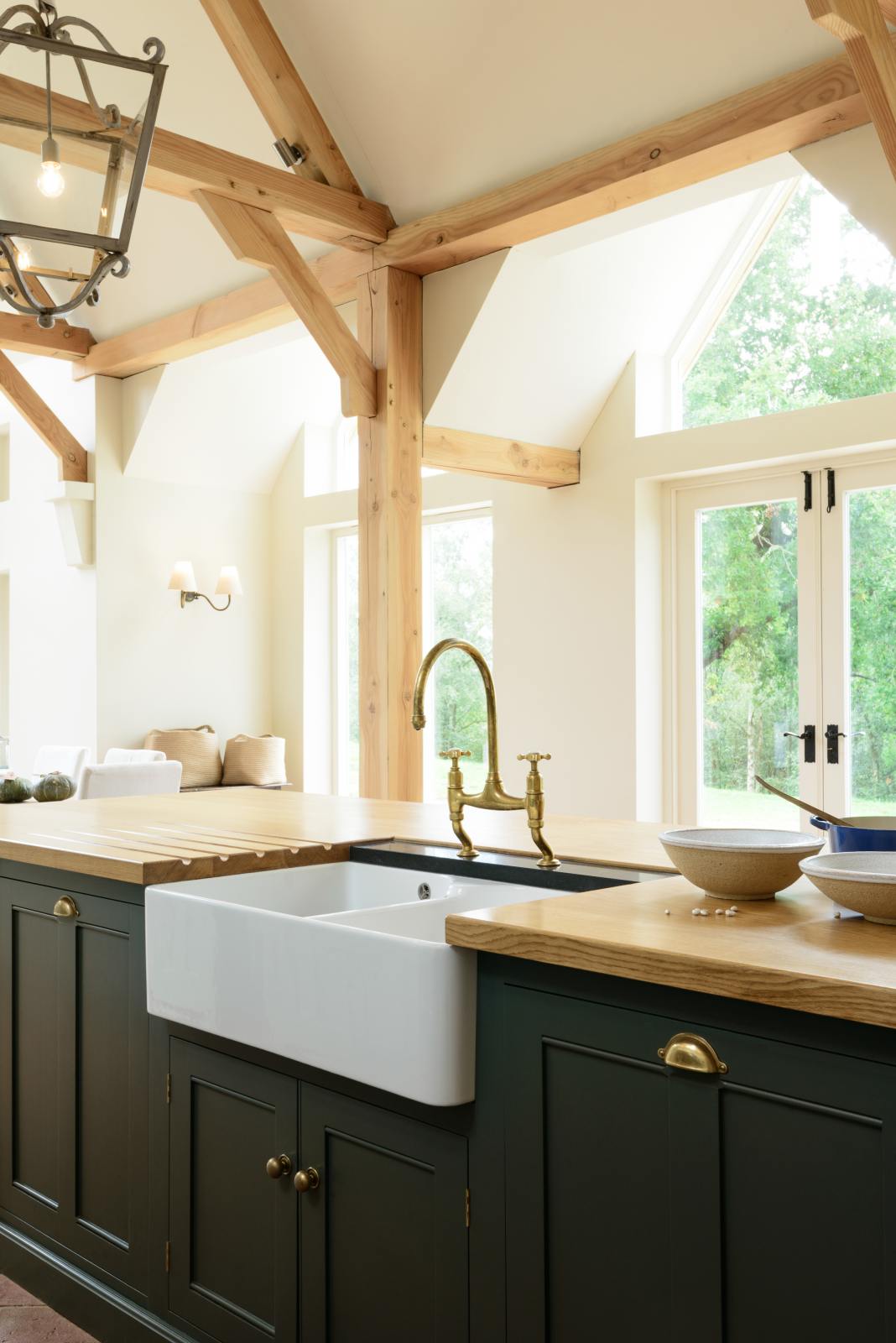 A closer look at an oak-framed barn kitchen’s kitchen island complete with a single Belfast sink and an aged brass Ionian tap atop a solid oak worktop. Adorned with framed pendant lights, artisan ceramics, weaved baskets, and pumpkins, this kitchen creates a warm and inviting space.