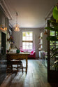 An eclectic, navy blue, classic English kitchen features a short and humble sink run, cooker run and a freestanding cabinet. The long, corridor-like space of a Georgian townhouse is beautifully decorated with beloved vintage items and furniture, paintings, copper pendant lights and unique kitchen equipment, giving the room a lot of whimsy, character and functionality.