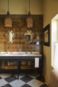 A beautiful butter-yellow powder room, you’ll find a black twin Victorian washstand, tall sepia lace market tiles, and a Parisian chequered marble floor. Paired with antique mirrors, pendant lights, vintage paintings, and framed pressed botanical artworks, the room exudes a glamorous, vintage charm.
