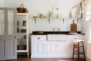 The simple and functional linen white scullery room with a modest sink run with polished sapele, a large single Carrara marble sink, and aged brass Mayan taps. The warm reds and browns of the terracotta square tiles, vintage furniture, ceramics, woven baskets and a deVOL laundry maid serve the room with both a purpose and beautiful aesthetics.
