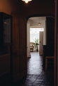 An angled, moody image of an archway, going from a dark and atmospheric corridor towards the white natural light through the Georgian windows. It emphasises the handmade textures of the terracotta square tiles that connect each room, creating a cohesive interior design.