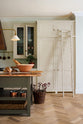 One side of a grand, earth-toned classic kitchen features a Silestone worktop cooker run, glazed wall cupboards, a full-height pantry, a copper canopy, a large island with a copper worktop, and a ladder. Adorned with warm colours such as an aged brass hanging rail, deVOL Heirloom gaselier lights, textured woven baskets, vintage ceramics and loaves of bread, it makes a spectacular use of space but also down-to-earth.
