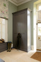 A quiet corner of a functional, muted-grey boot room features an L-shaped bench and a full-height storage cupboard. Beautifully decorated with thick coats, a stack of hats, and a pair of muddy boots, it creates a practical and family-oriented space.