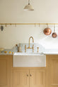 A closer look at a charming blush yellow, classic English kitchen features a Carrara marble countertop, an ornate backsplash, and an aged brass tap. Decorated with copper pots, vintage ceramics, and small wooden cleaning supplies, it creates an elegant and tidy atmosphere.