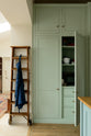 A corner of a humble and calming turquoise, classic English kitchen featuring a large full-height pantry cupboards with top cabinets, and a wooden ladder. Adorned with navy blue apron, a small rice cooker, and a silver cheese grater, it creates a warm and simple home kitchen.