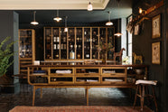 A cool and elegant Haberdasher’s collection features a large prep table with a copper worktop, a pantry run with tambour base cabinets, glazed countertop cabinets, and a freestanding pantry with glazed doors. Adorned with vintage furniture and items, artisan ceramics, the deVOL porcelain light collection, Creedy stools, assorted containers, bottles, and a stunning bouquet of dried flowers, this space creates an atmospheric social bar.