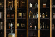 A closer look at a cool and elegant Haberdasher’s collection featuring a pantry run with glazed countertop cabinets. Adorned with vintage items, assorted containers, and bottles, this space creates an atmospheric social bar.