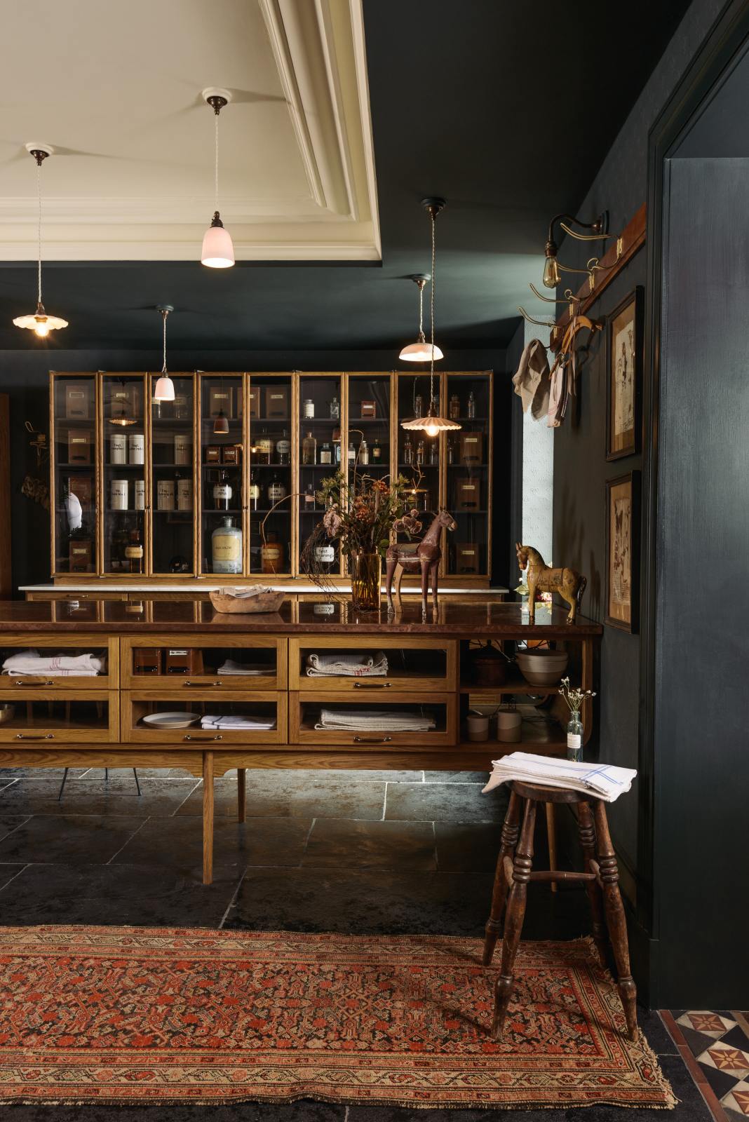 A cool and elegant Haberdasher’s collection features a large prep table with a copper worktop, a pantry run with tambour base cabinets, and glazed countertop cabinets. Adorned with vintage furniture and items, artisan ceramics, the deVOL porcelain light collection, assorted containers, and bottles, this space creates an atmospheric social bar.