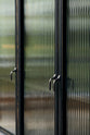 A close and oblique view of a bobbin black Haberdasher’s wall cupboard with reeded glass and oxidised brass pull hooks.