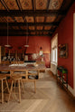 A warm and historical Haberdasher’s kitchen features a sink and cooker run with red Zellige splashback tiles, a kitchen island with an aged brass Ionian tap, and a red marble worktop. Beautifully decorated with decorative floral ceiling tiles, large narrow pleat porcelain lights, Helen stools, artisan ceramics, vintage items, and paintings, this kitchen creates a grand yet comfortable space.