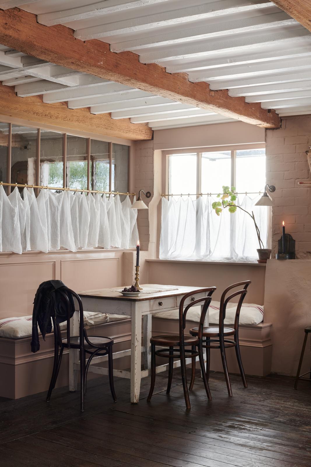 Past the refectory-red Heirloom kitchen is a spacious dining area adorned with vintage furniture. Beautifully decorated with a Heirloom wall light, aged brass café curtains, luscious green house plants, and cherished candlesticks, this space offers a modern twist on vintage aesthetics, creating a classic space designed to endure.