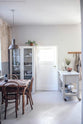 A vintage square dining table with chairs and a glass storage cupboard, complemented by a small rolling kitchen island with Carrara marble worktop to serve humble meals.