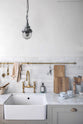 A closer look at the humble Mushroom colour shaker kitchen with an all-in-one L-shaped sink and cooker run, and a small rolling kitchen island with Carrara marble worktop. A single Belfast sink is complemented by an aged brass Ionian tap, and an aged brass hanging rail adds a striking element against the grey and neutral tones of this charming kitchen.
