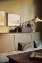A close-up of a simple buttery yellow Shaker living space features a Folgate green bespoke bench seat with an open base cabinet, a rise and fall pendant light, an amber glaze teapot, and a cohesive set of vintage table and chairs. Lovingly adorned with artisan ceramics, paintings, books, a coat rack and cushions, creating a cosy and Mediterranean cafe-inspired social space.