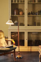 A close-up of a simple buttery yellow Shaker living space features a Quaker cream curiosity cupboard, a grand tour reading lamp, and a cohesive set of vintage furniture. Lovingly adorned with artisan ceramics, books, and antique canes, creating a humble and mid-century inspired social space