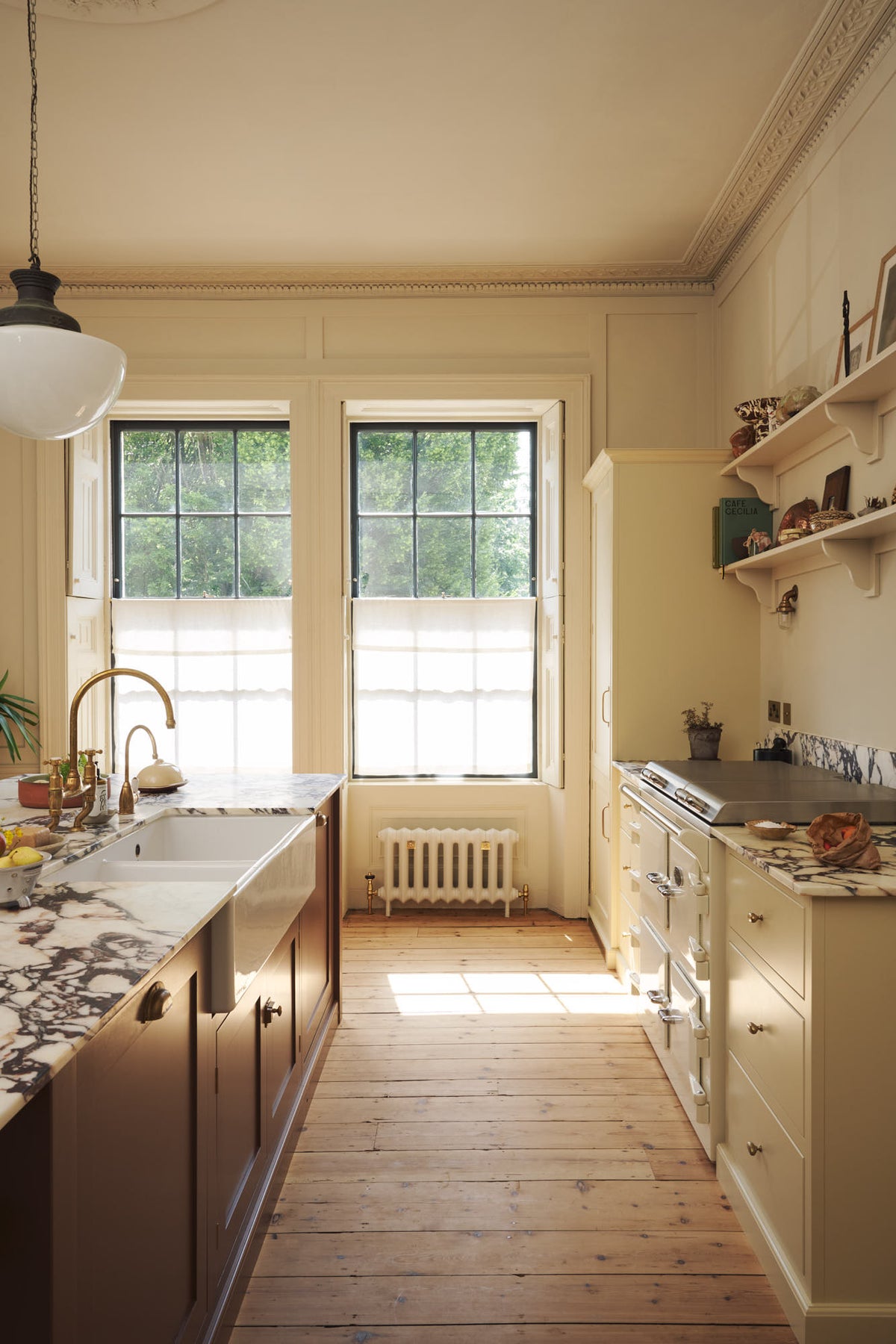 A bright, spacious, warm, and simple-yet-grand shaker kitchen featuring a large kitchen island with a Calacatta Viola worktop, a cooker run, a fridge/freezer cupboard, and long shaker shelves. Perfectly decorated with beloved vintage furniture and decor made from different natural materials, it creates a scene of absolute beauty, personality and functionality.
