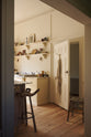 An oblique view of a bright, spacious, warm, and simple-yet-grand shaker kitchen featuring a large kitchen island with a Calacatta Viola worktop, a cooker run, and long shaker shelves. Perfectly decorated with beloved vintage furniture and decor made from different natural materials, it creates a scene of absolute beauty, personality and functionality.