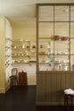 A simple Quaker cream and Folgate green Shaker scullery features architectural glazed partitions, bespoke shelving, and a sink run with a Silestone worktop, finished with a cream subway tiles splashback. Lovingly adorned with artisan ceramics, wooden chopping boards, and antique kitchen accessories and furniture, it gives a sombre and practical space.