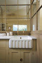 A close-up of a simple Quaker cream and Folgate green Shaker scullery features architectural glazed partitions, and a sink run with a Silestone worktop. Lovingly adorned with artisan ceramics, and aged brass Mayan taps, it gives a sombre and practical space.