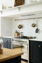 A closer look at the pantry-blue shaker kitchen’s cooker run, built into a chimney breast with a Silestone worktop, white porcelain splashback tiles, and an aged brass hanging rail.