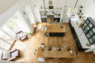 An almost bird’s-eye view from the balcony reveals a pantry-blue shaker kitchen, where solid oak parquet floors and rusty metal pendant lights bring texture and an industrial edge. The space features a sink run with a Silestone worktop, a large solid oak-topped island with glazed cupboards, and a vintage oak dining table with wooden benches and mismatched chairs for added character.