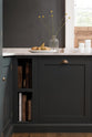 A quiet corner of a charcoal-black, classic shaker kitchen features a U-shaped sink and cooker run with Carrara marble worktop. Beautifully decorated with wooden chopping boards, charcuterie boards, plastic cups, a glass vase of flowers, fresh pears, and the original Georgian wooden sliders, the family kitchen strikes a wonderful balance between modern style and timeless character.