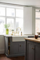 A closer look at a simple, modern shaker kitchen in a historic Cheshire townhouse, featuring a Silestone sink run with a Belfast sink and aged brass Ionian tap, and a large island with a solid oak worktop and a breakfast nook. Painted in muted cool grey with white walls and warm terracotta tile flooring. 