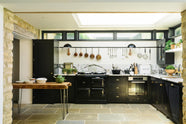 This beautifully renovated kitchen features a Painter’s Black shaker style with an L-shaped layout that includes a cooker and sink run. The worktop and splashback are made from San Simone quartzite, complemented by an overhead glazed cupboard and a tall storage cupboard. A glass skylight brightens the modern space while honouring the historical character of the building by retaining the original brick wall.