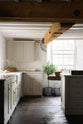 A closer look at the sink run in a simple English farmhouse kitchen at deVOL’s headquarters, Cotes Mill. Low-exposed wooden beams and worn floorboards set a rustic tone, while textured off-white walls add character. The Shaker kitchen, including the island, is painted in Mushroom—a soft, timeless beige.