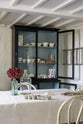 An angled view of deVOL’s custom cupboards painted in Pantry Blue, contrasting sharply with the light Ocean Trinity Blue interior. Lovingly styled with white ceramic bowls, cartons of eggs, cookbooks, and a large seashell collection.