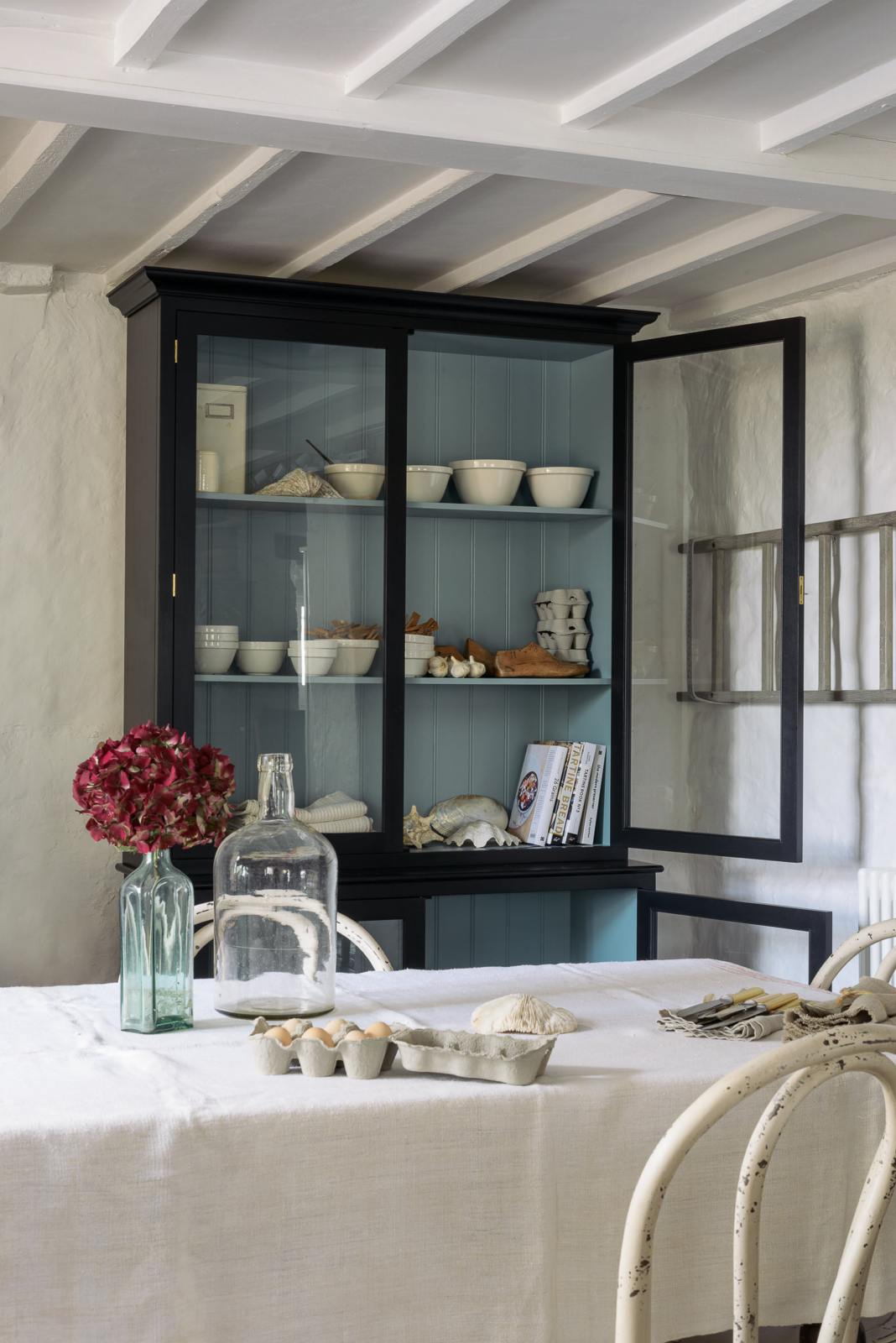 An angled view of deVOL’s custom cupboards painted in Pantry Blue, contrasting sharply with the light Ocean Trinity Blue interior. Lovingly styled with white ceramic bowls, cartons of eggs, cookbooks, and a large seashell collection.