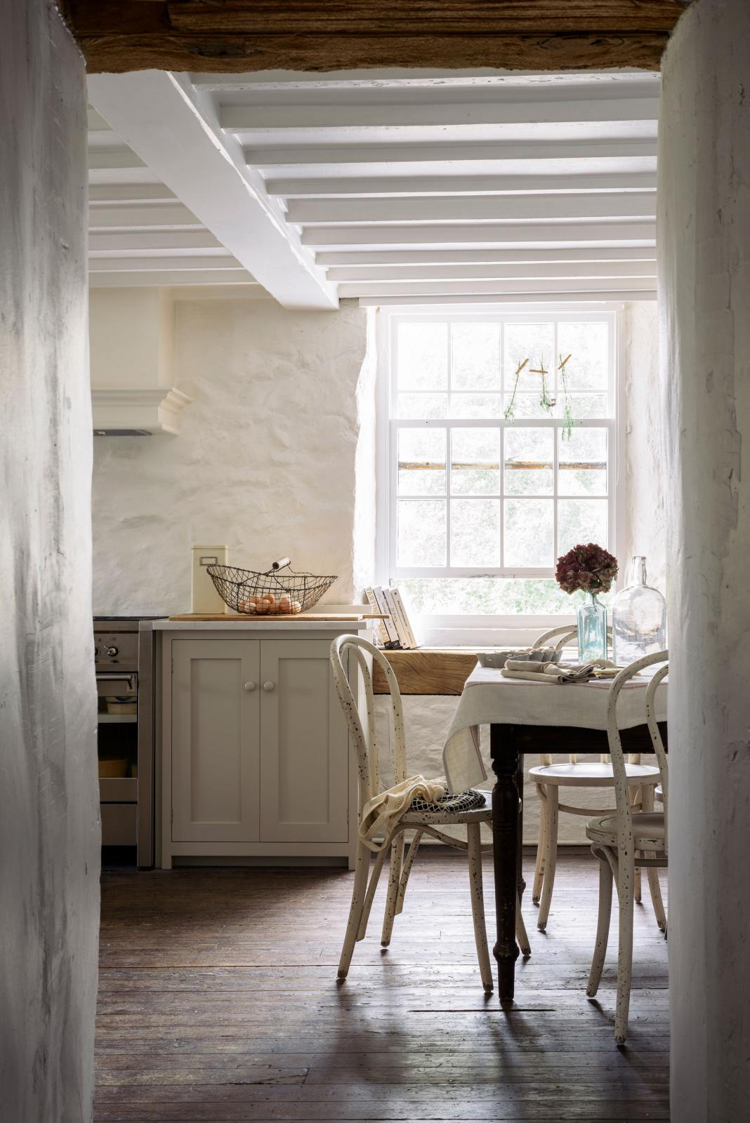 An atmospheric image of bright white light filling a simple English farmhouse-style kitchen with assorted vintage furniture, located at deVOL’s headquarters in Cotes Mill. The room features low, exposed wooden beams and worn wooden floorboards.