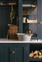 A closer look at the wooden and metal accents—including firewood, a metal bin, and a wooden toolbox of the pantry blue shaker kitchen’s sink run features a shelf, countertop glazed cupboards, a mix of closed and open base cabinets and a Carrara marble worktop.