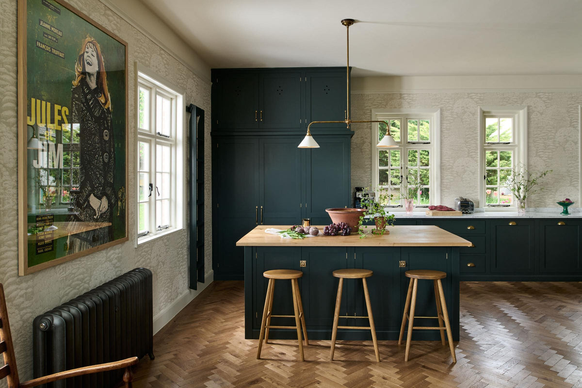 This spacious Bakehouse Green shaker kitchen features a sink run and a concave cooker run, complemented by a Carrara marble worktop. It features a solid oak parquet floor, a floor-to-ceiling pantry, and a modest kitchen island with a solid oak worktop that serves as a breakfast bar, with three iconic Helen stools.