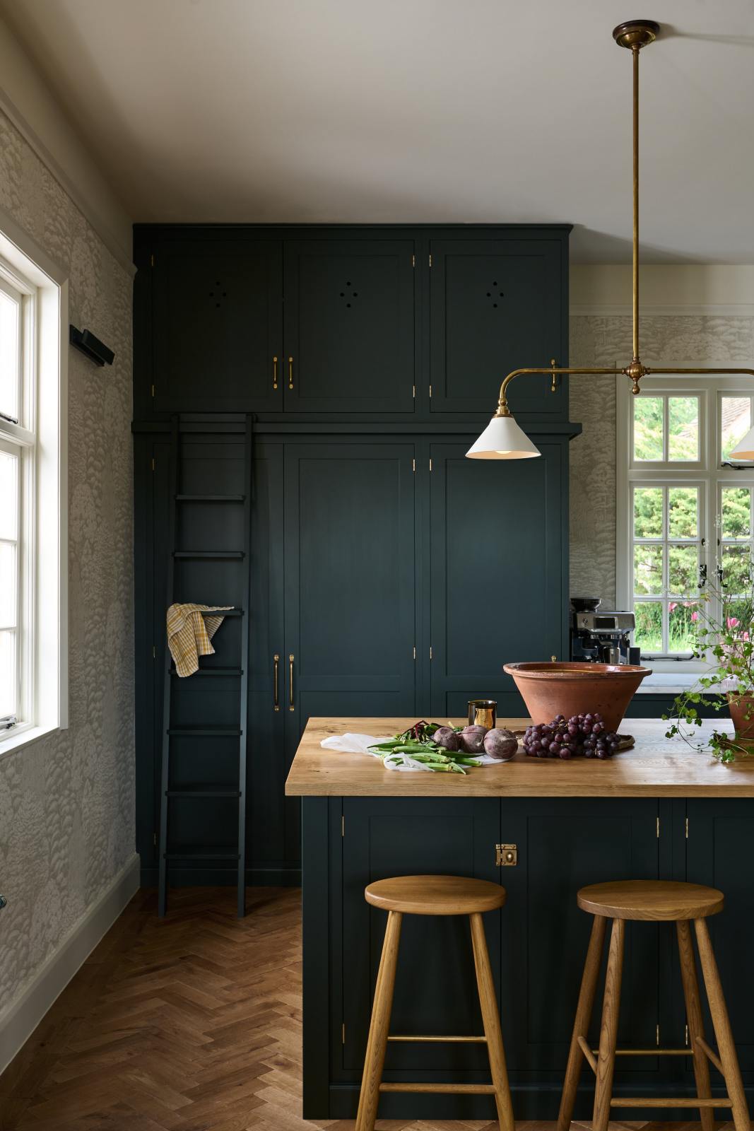 A closer look at the floor-to-ceiling pantry, which features a bespoke ladder, along with a modest kitchen island topped with solid oak that serves as a breakfast bar equipped with two iconic Helen stools.