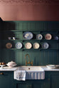 A straight-on close-up of tongue-and-groove panelling and shelving above deVOL’s 800mm single-bowl ceramic sink with a fluted front. Vintage blue and white willow pattern plates line the shallow Shaker shelves with elegant charm.