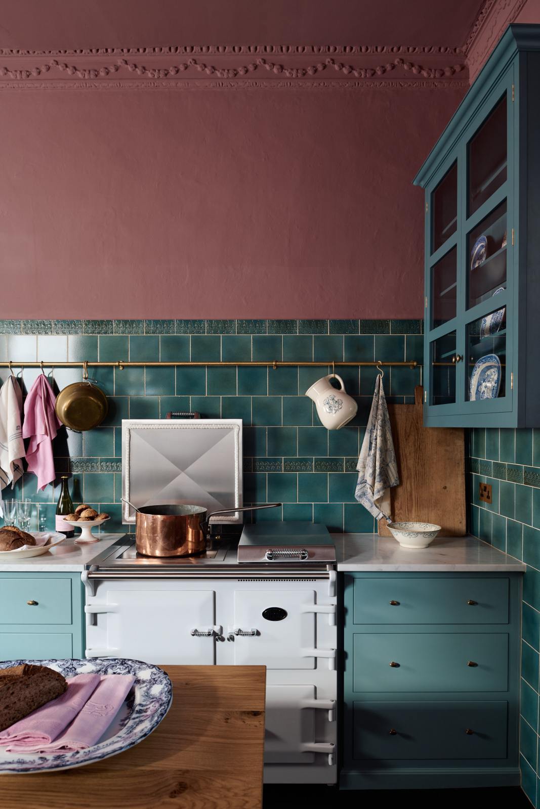 The cooker run in this kitchen sits in the corner of the room in a Clerkenwell blue Shaker pan drawers on either side of the classic white Aga range cooker. Each unit has three drawers, the top drawer slightly shorter than the bottom two, and each drawer is finished with two delicate brass oval knobs.