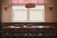 A grand, refectory red dining room with a Millhouse refectory table, Bentwood café chairs and a bench. The table is adorned with red beets and leaves, sea-green heirloom platters, a vintage red-and-white striped chandelier, and red-rimmed wall lights.