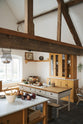 A Scullery Yellow Shaker kitchen with a compact sink run featuring a Carrara marble worktop, a single Belfast sink with aged brass Mayan taps, a full-height cabinet, Shaker shelves, and an L-shaped Shaker bench seat. The space also includes a kitchen island and a closed larder with glazed cupboards. Vintage furniture and beloved items, such as mixing bowls and fresh produce, add character. The high ceilings retain their original exposed wooden structure.