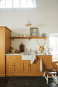 A scullery yellow shaker kitchen with a small sink run with a Carrara marble sink, a full-height cabinet, shaker shelves and an L-shaped shaker bench seat. The kitchen features a single Belfast sink with aged brass Mayan taps, a collection of vintage furniture and beloved items.