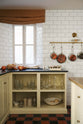 A traditional-style scullery, with pale yellow painted Shaker open base cupboards and walls covered in simple white metro tiles.