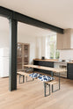 An oblique view of a simple and contemporary Sebastian Cox kitchen’s cooker run with a canopy, and a solid oak worktop. Adorned with bare pendant lights, a silver electrical hob, a black marble utensil holder, and a white refrigerator, this kitchen creates a cosy space with industrial details and a practical finish.